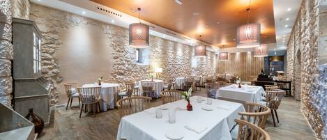 Ein Restaurant mit Steinsäulen, Holztischen und hängenden Lampen.