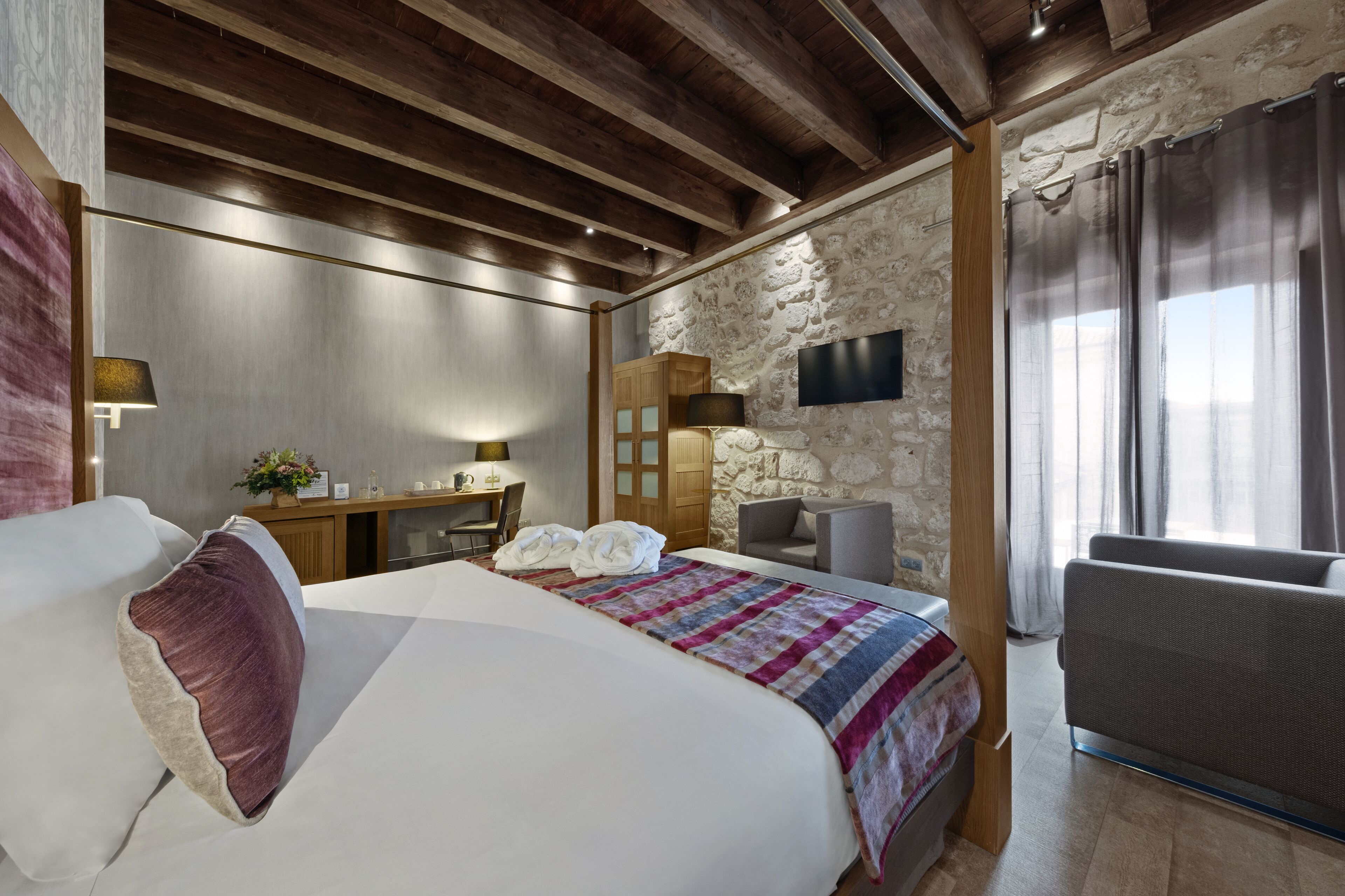 Een slaapkamer met een groot bed, een bureau, een stoel, een televisie en een stenen muur.