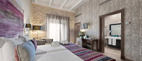 A hotel room with a large bed, a desk, a TV, and a stone wall.