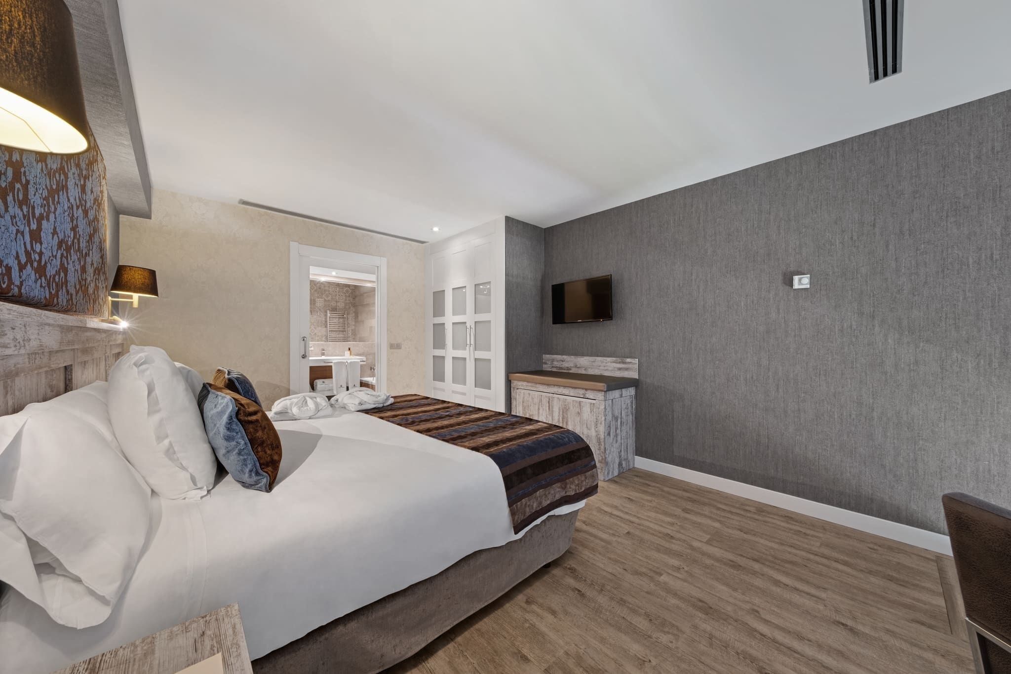 Une chambre d’hôtel moderne dotée d’un grand lit, d’un bureau, d’une télévision à écran plat et d’une salle de bain visible à travers une porte ouverte.