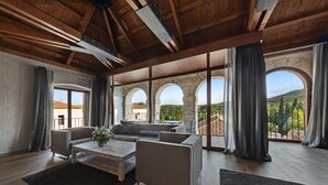 A spacious living room with a wooden ceiling, large windows, and a view of a courtyard with arches.