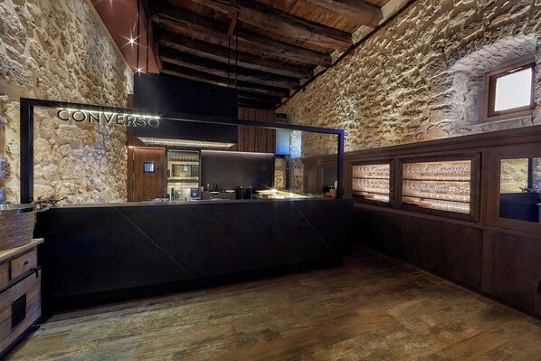 A stone-walled interior with a black reception desk, wooden beams, and a window with a view.