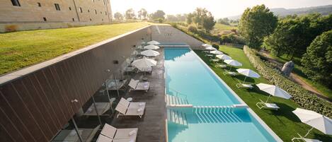 A swimming pool with lounge chairs and umbrellas, surrounded by a stone wall and a grassy area.