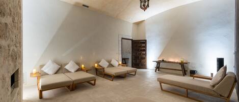 A spacious room with a high ceiling, a fireplace, and a seating area with cushions and a table.