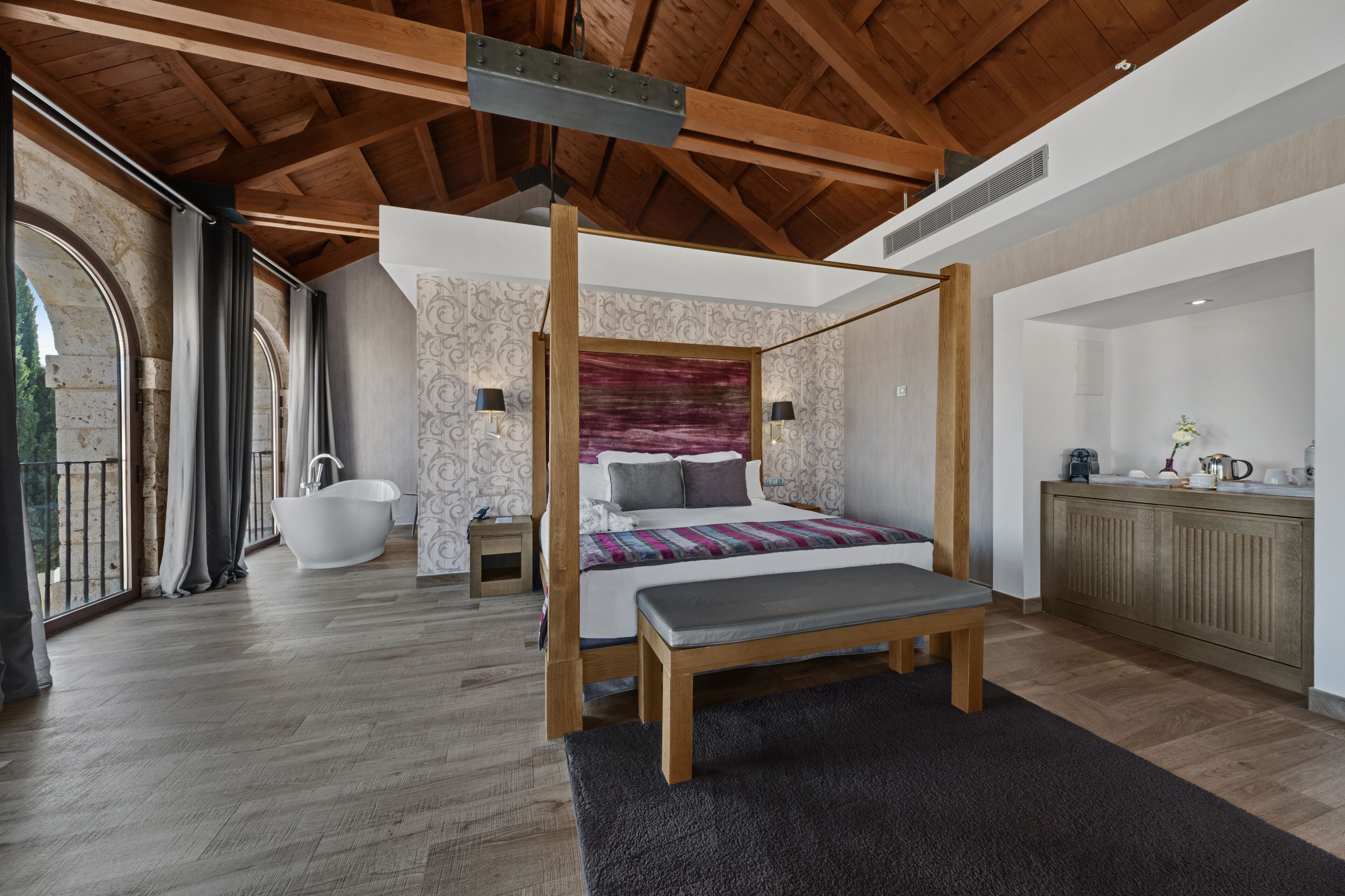 Un espacioso dormitorio con cama con dosel, techo de madera y un gran ventanal con cortinas.