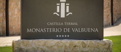 Un cartel del Monasterio de Valbuena, Castillo Termal, con base de piedra y diseño sencillo.