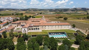 A large estate with multiple buildings, a swimming pool, and vineyards in the background.