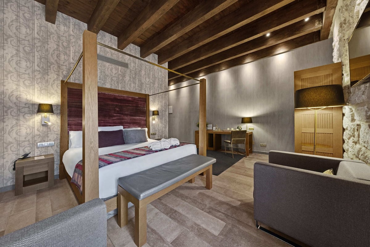 A bedroom with a four-poster bed, a desk, a chair, and a bench.