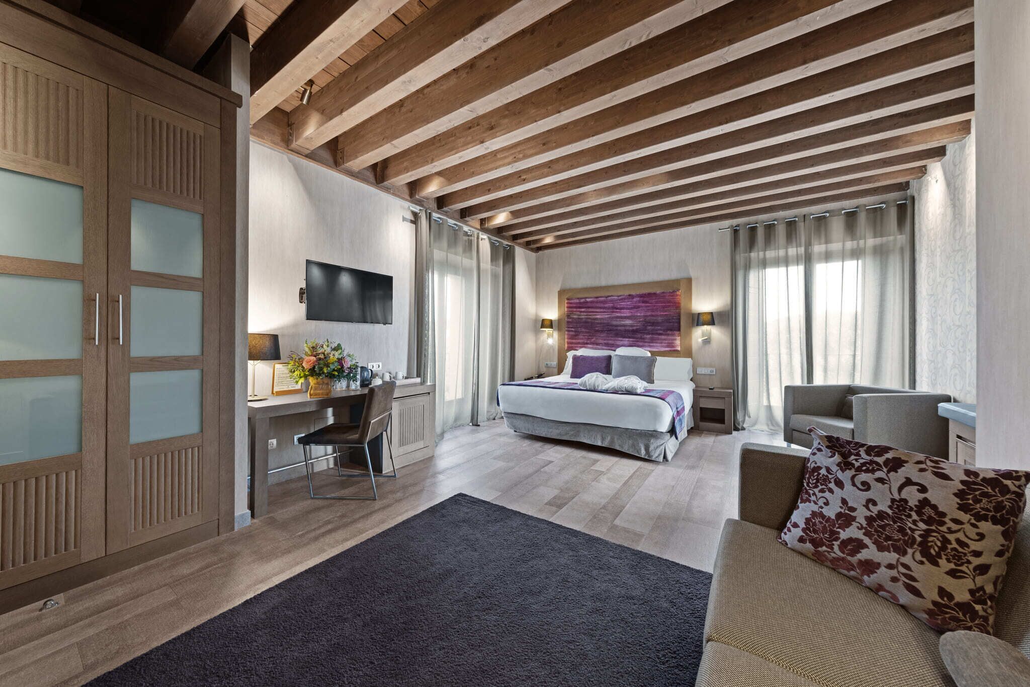 A modern bedroom with a bed, a desk, and a TV.