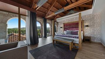 A bedroom with a large bed, wooden beams, a balcony, and a view of the countryside.