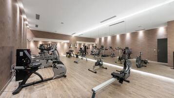 A spacious gym with various cardio and strength training equipment, a large mirror wall, and a wooden floor.