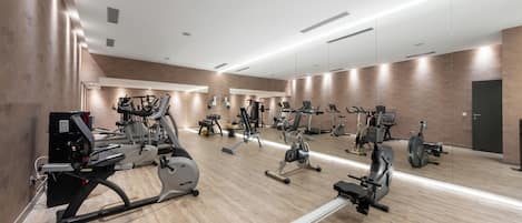 A spacious gym with various cardio and strength training equipment, a large mirror wall, and a wooden floor.
