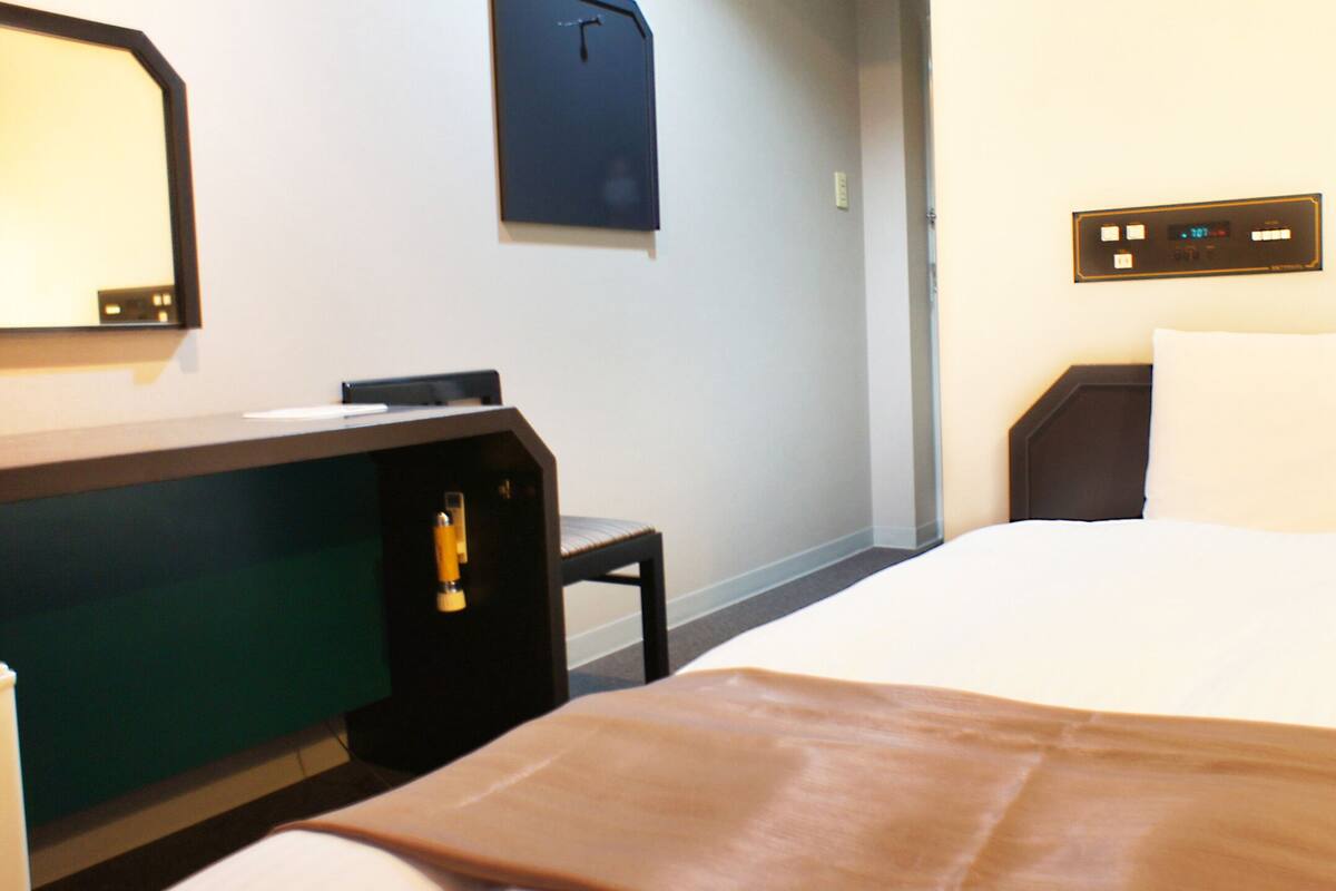 Ein Hotelzimmer mit Bett, Schreibtisch, Stuhl, Spiegel und Bedienfeld an der Wand.