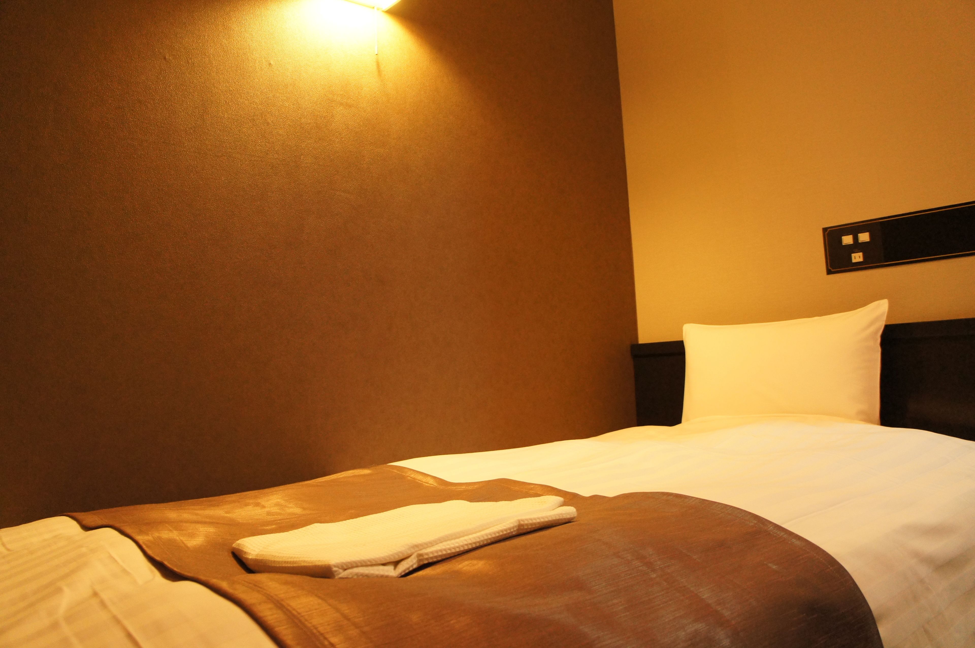 Una habitación de hotel con una cama bien hecha, una mesita de noche y una lámpara fijada a la pared.