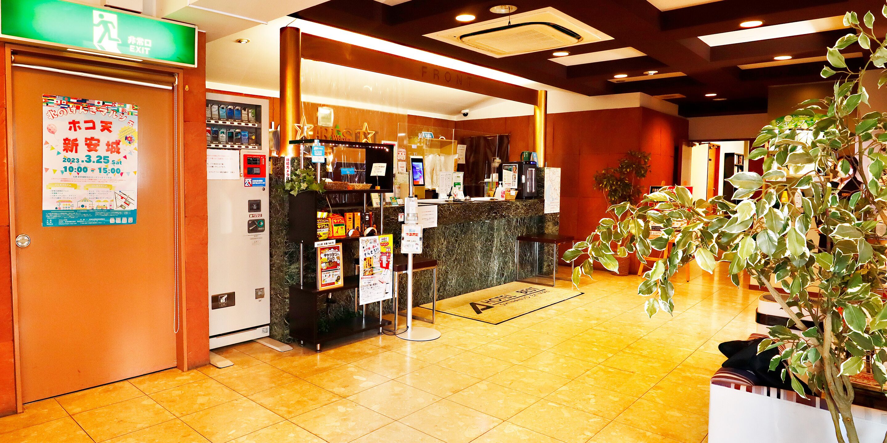 A hotel lobby with a reception desk, vending machines, and a plant.