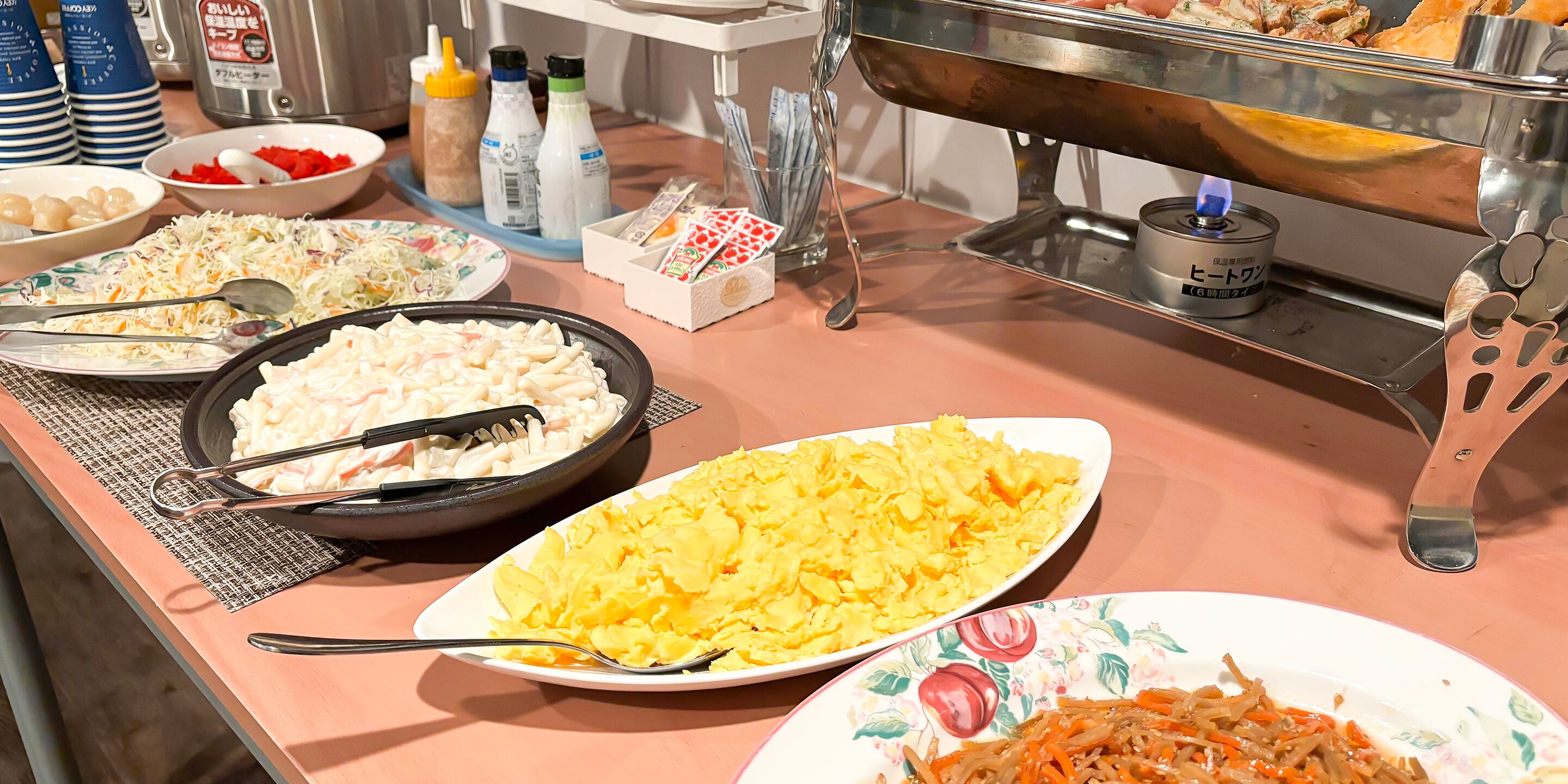 A buffet table with various dishes including coleslaw, scrambled eggs, and other prepared foods.