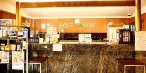 Un comptoir d’accueil d’hôtel avec un revêtement en marbre, une machine à café et divers panneaux d’information.