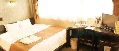 A hotel room with a bed, a desk, a chair, a TV, and a trash bin.