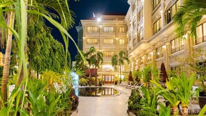 A well-lit hotel courtyard with a central reflecting pool, surrounded by lush greenery and palm trees. - Monoreach Angkor Hotel (Siem Reap)