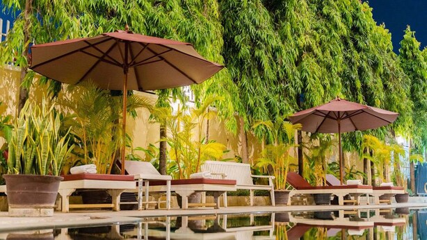 A poolside area with lounge chairs and umbrellas, surrounded by lush greenery. - Monoreach Angkor Hotel (Siem Reap)