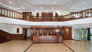 A spacious lobby with a wooden reception desk, a staircase, and a second-floor balcony. - Monoreach Angkor Hotel (Siem Reap)