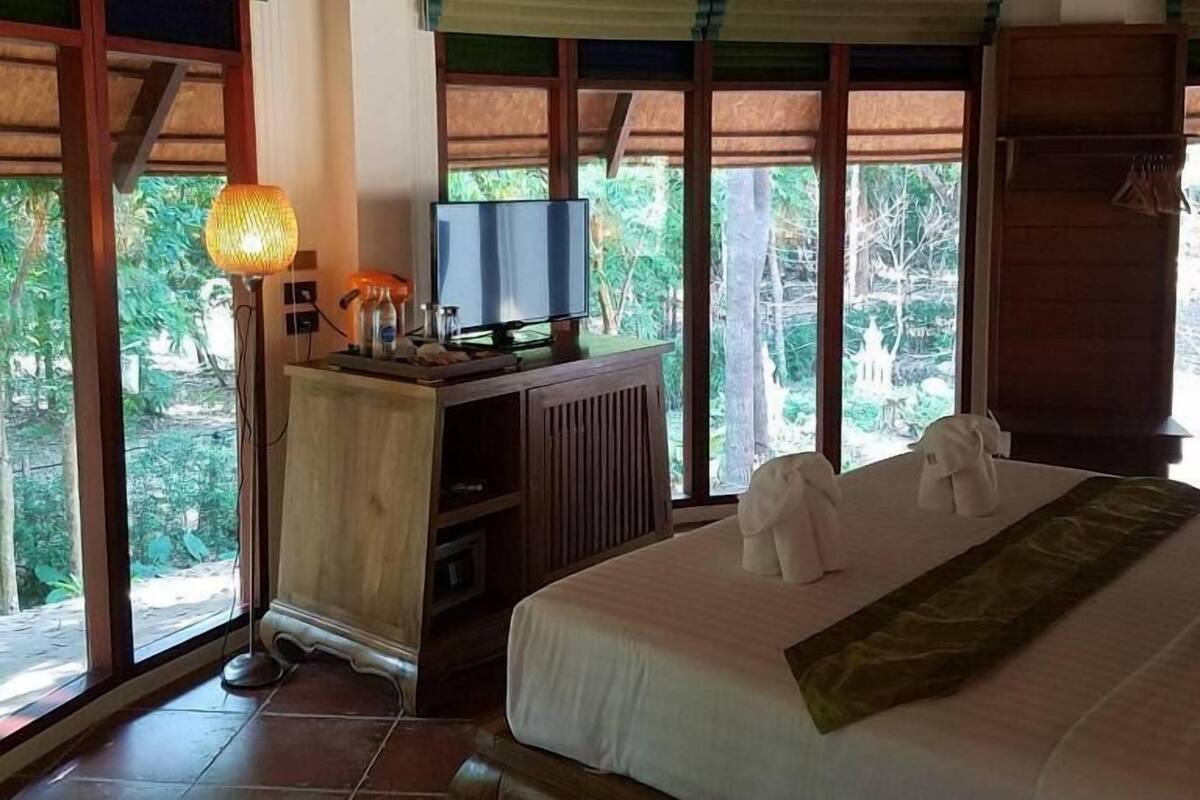 A bedroom with a bed, a desk with a television, and windows with curtains.