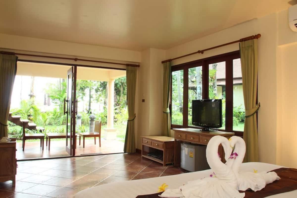 A hotel room with a bed, a desk with a television, a sliding glass door to a garden, and a small table.