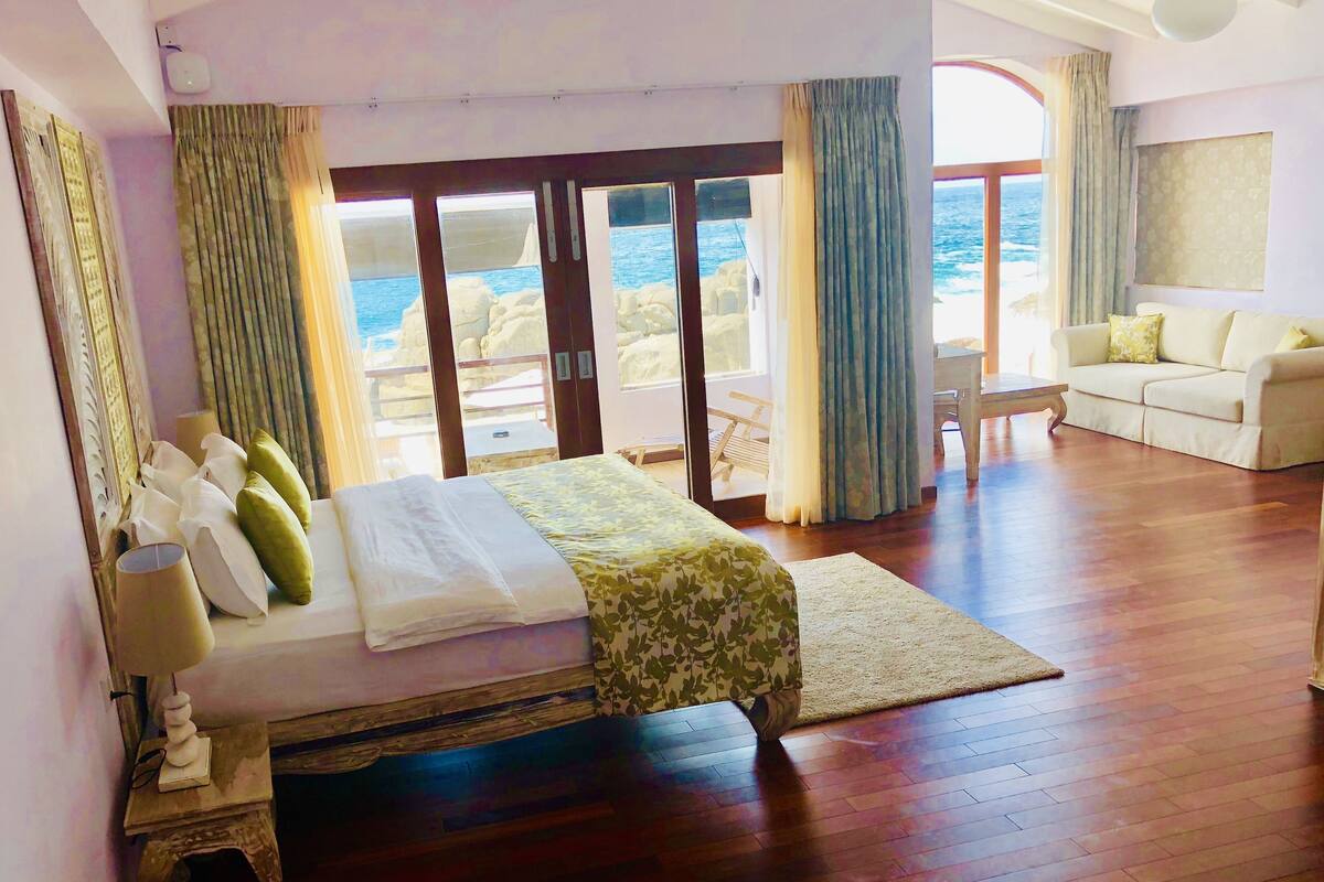 Quarto de hotel com cama, sofá, vista para o mar e varanda.