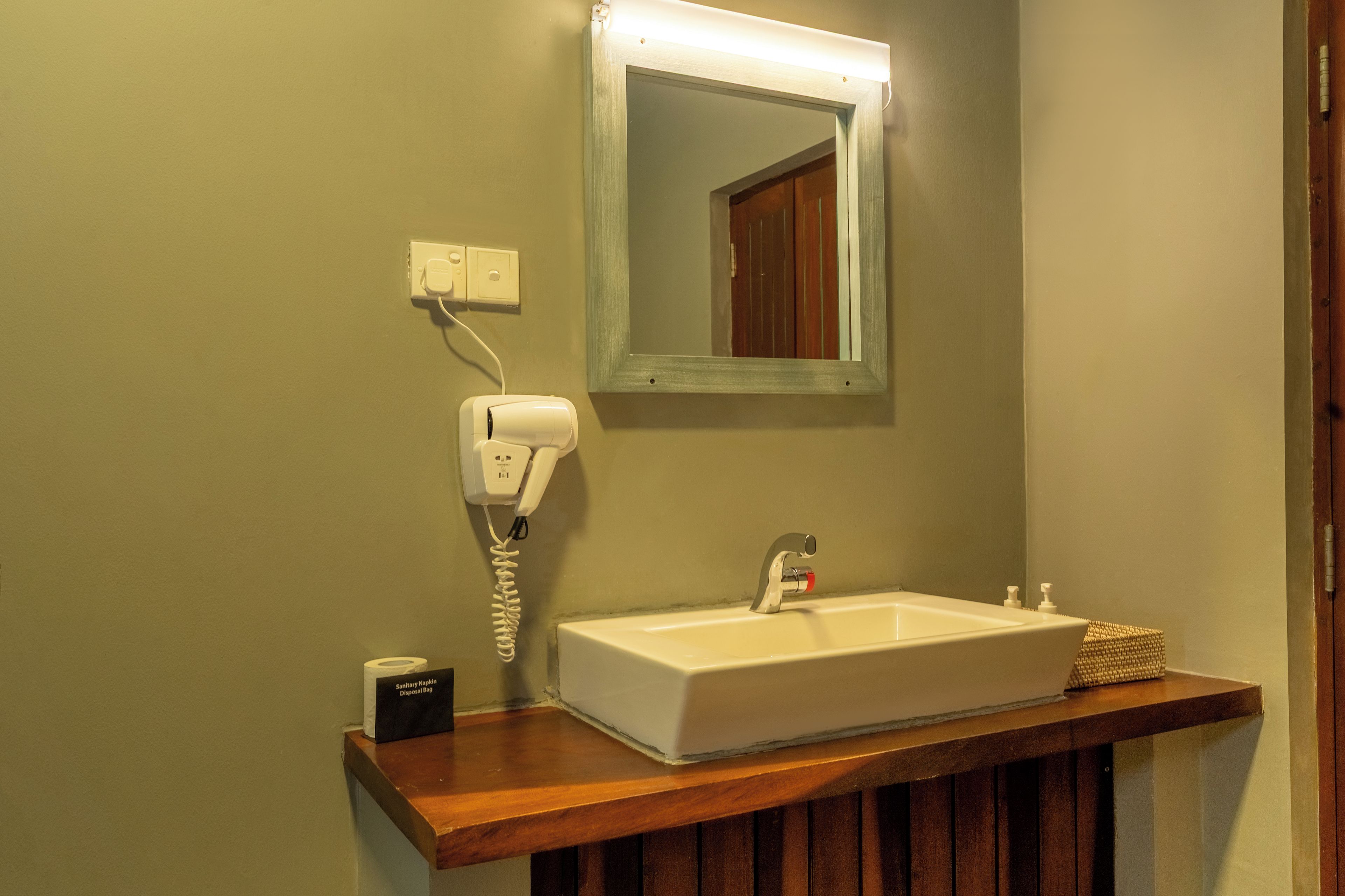 Une salle de bain avec un lavabo blanc, un miroir, un sèche-cheveux et une petite poubelle.