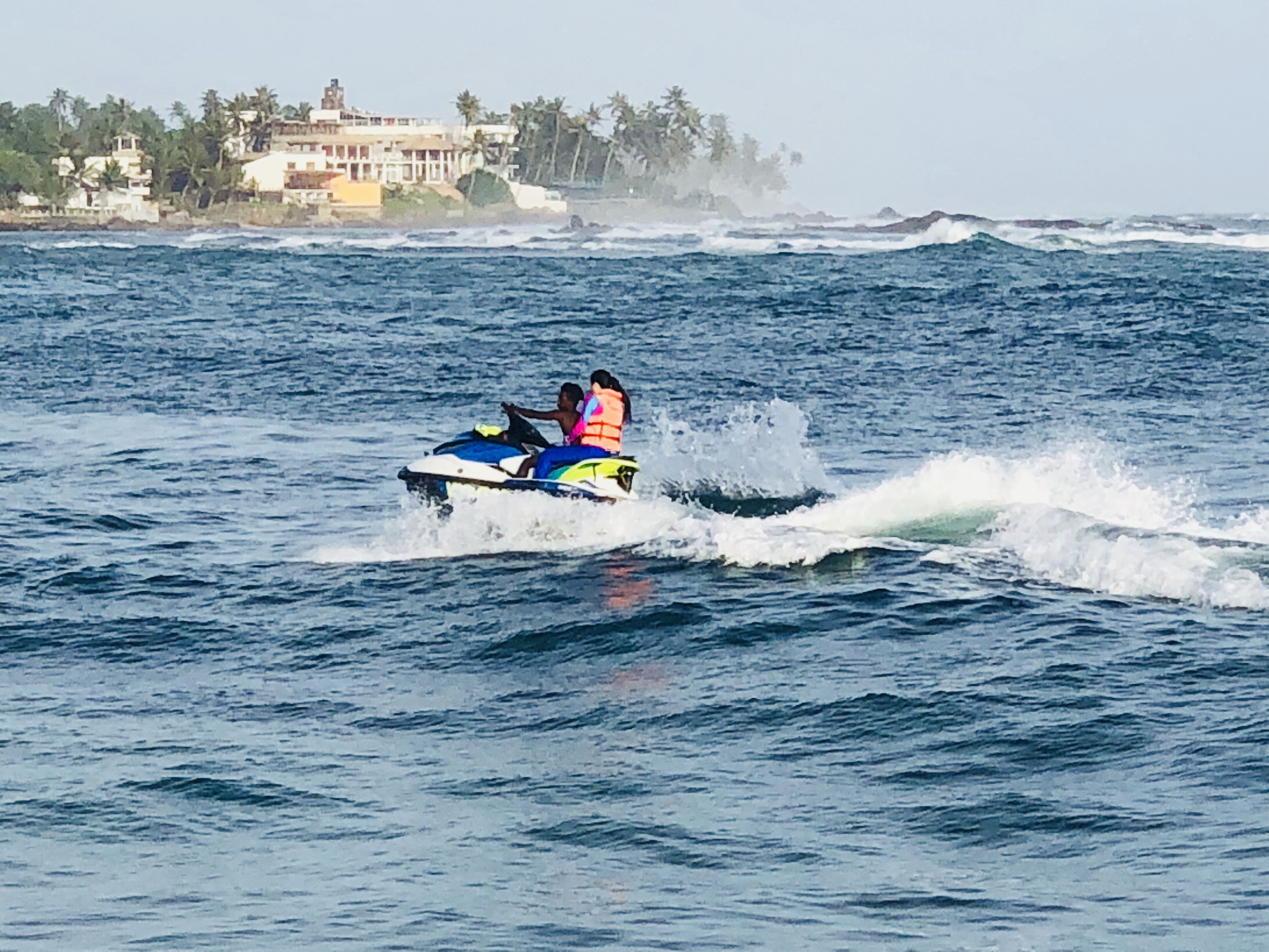 A jet ski on the water with a building and palm trees in the background.