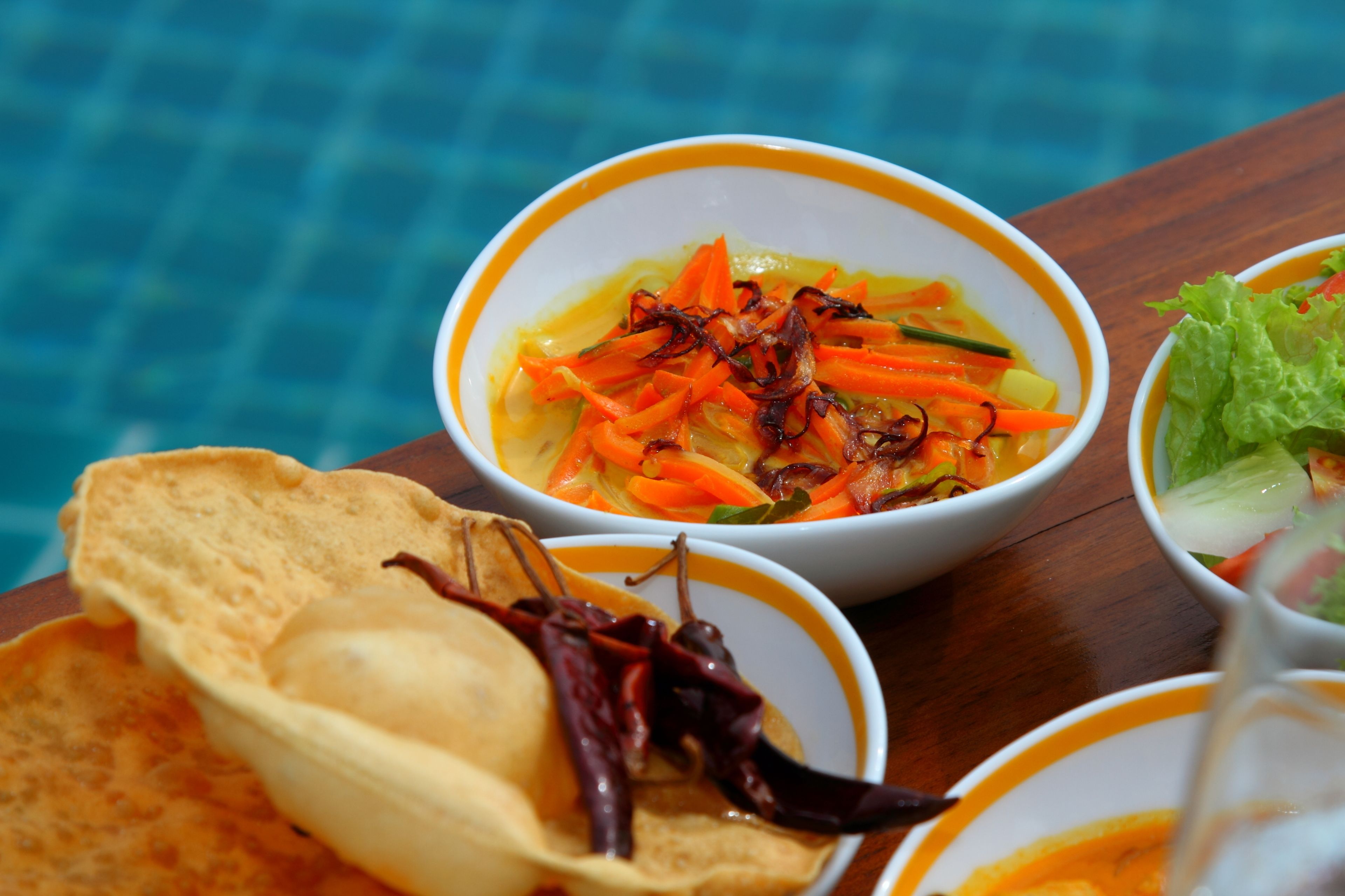 Une table avec des bols remplis de nourriture, notamment une soupe aux légumes et des aliments frits, ainsi qu’un saladier de salade.