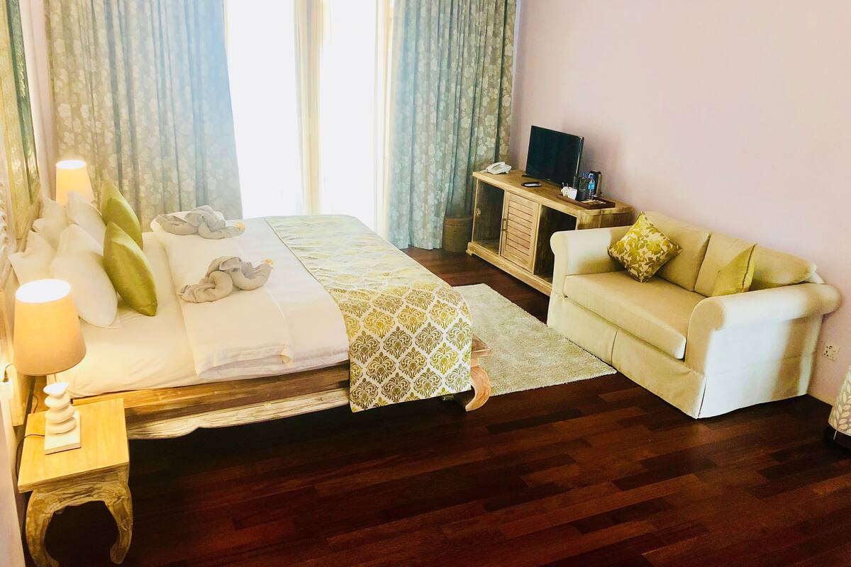 Quarto de hotel com cama, sofá, televisão e mesa de cabeceira com abajur.