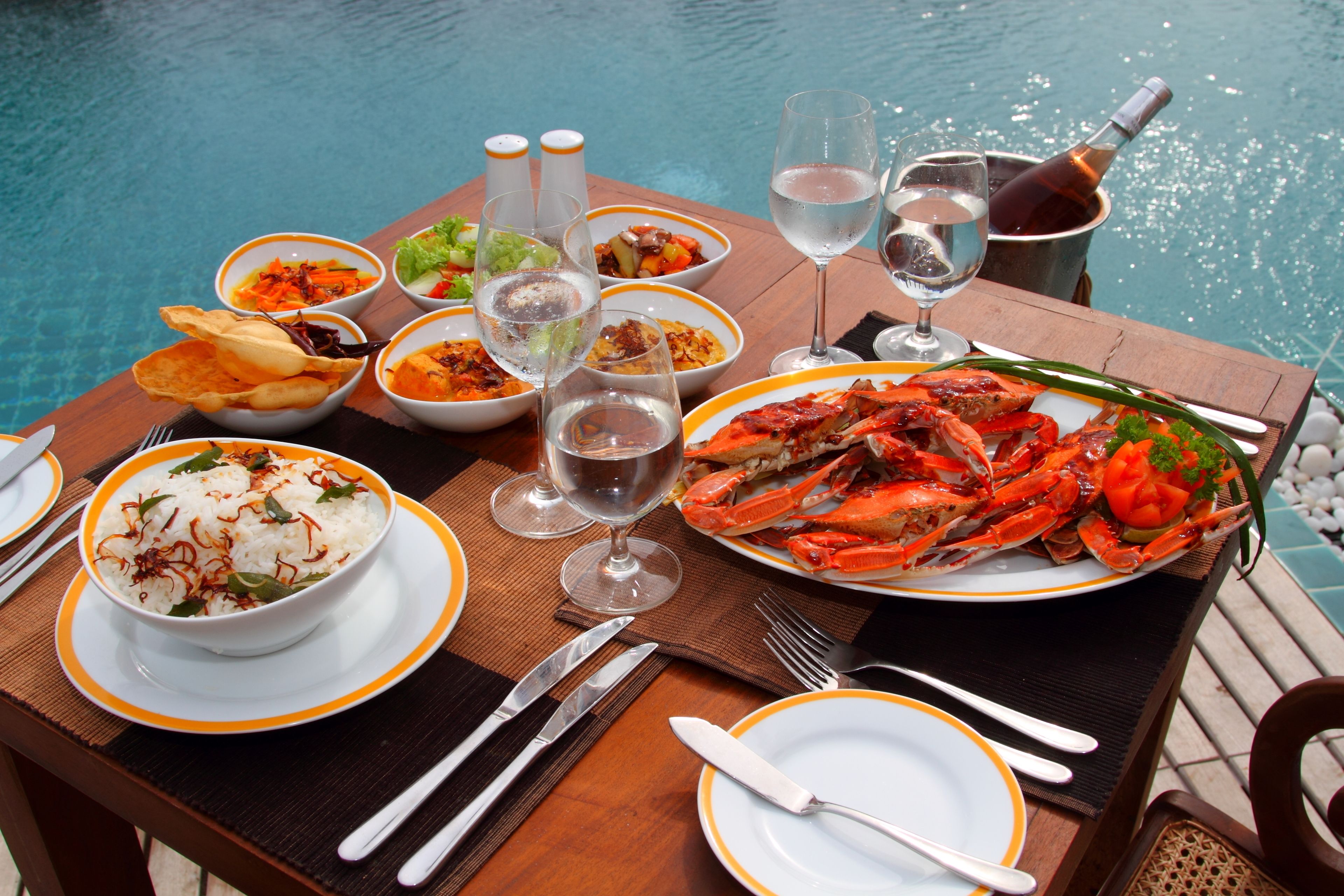 A dining table with various dishes, including seafood, rice, and vegetables, set by a pool.
