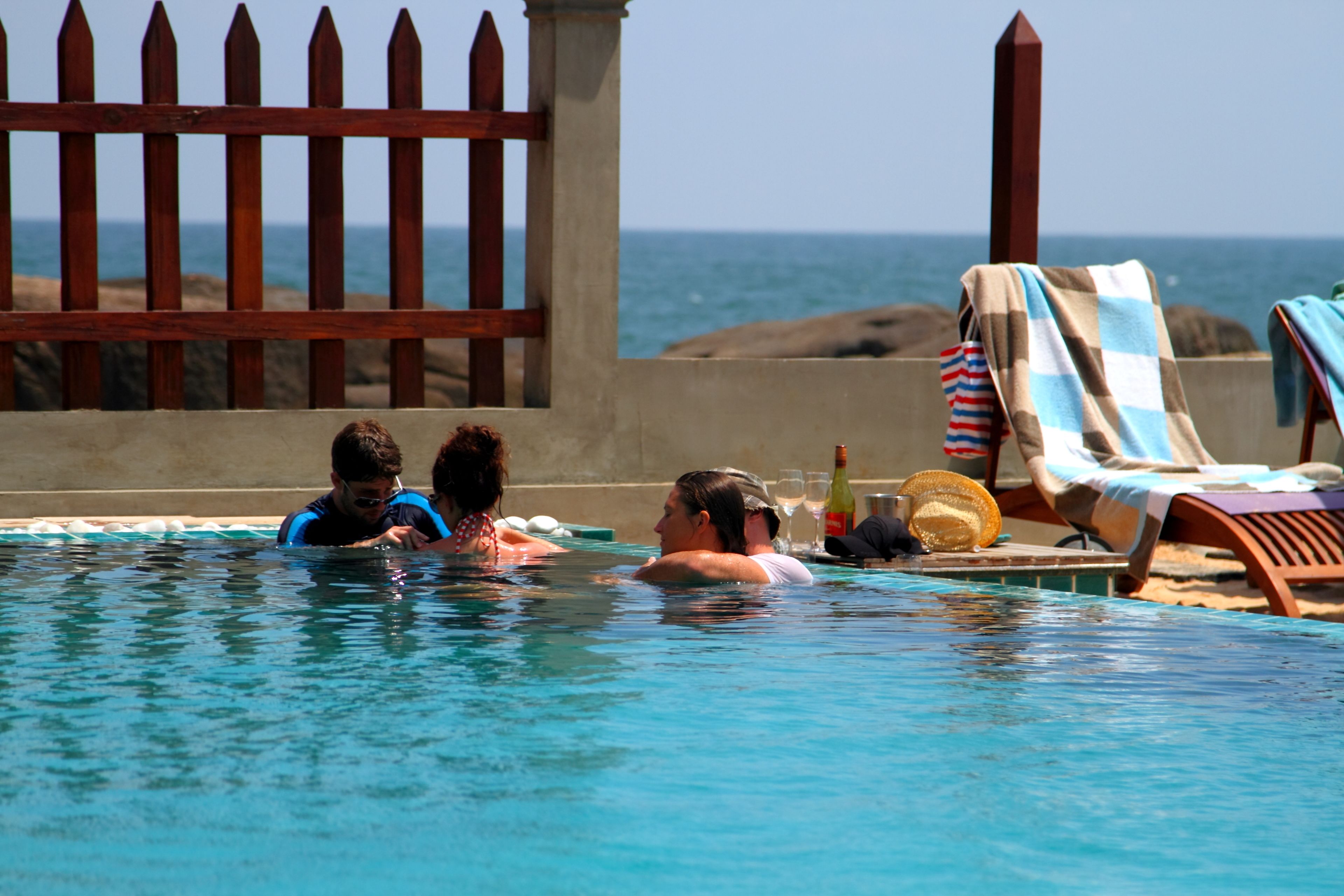 A swimming pool with a wooden fence, lounge chairs, and a view of the ocean.