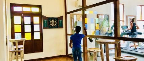 A room with a large window, wooden flooring, a dartboard, and a treadmill.