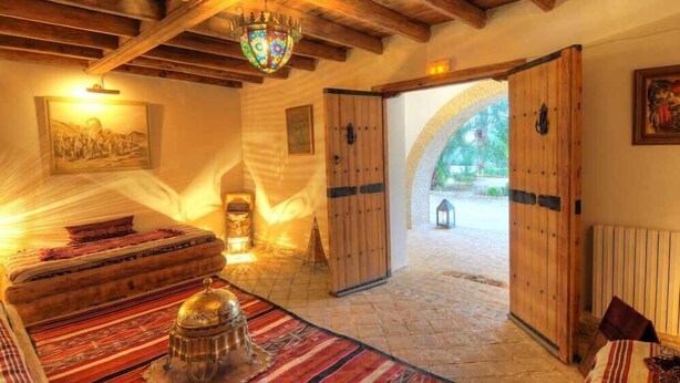 A traditional room with a bed, a chandelier, and wooden doors leading to an outdoor area. - Dar Zargouni (Nefta)