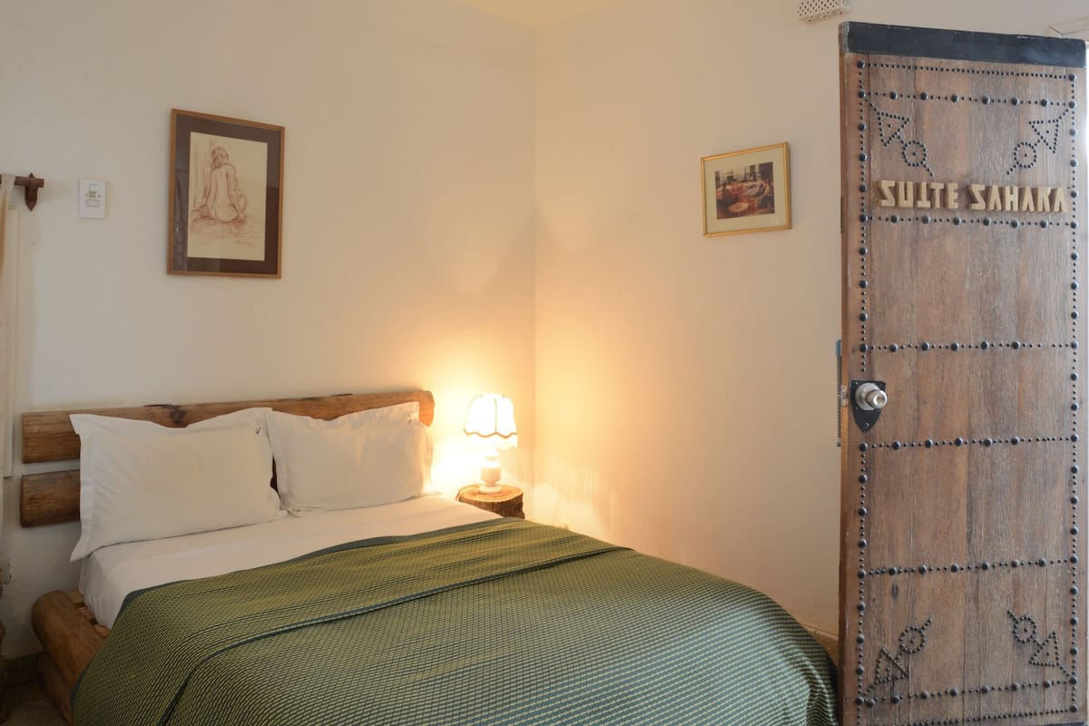 A bedroom with a bed, a nightstand, a lamp, a wooden door, and two framed pictures on the wall.