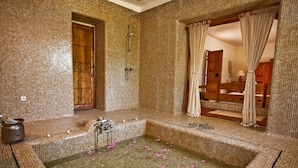 A bathroom with mosaic tile walls, a wooden door, a bathtub, and a shower area. - Dar Zargouni (Nefta)