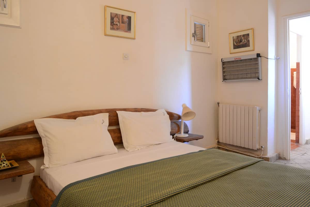 A bedroom with a wooden bed, white bedding, a green blanket, a bedside lamp, and a radiator.
