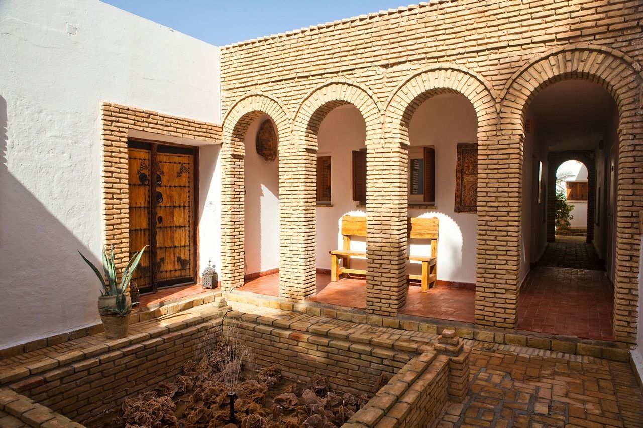 Un patio con pared de ladrillo, puerta de madera y arcos.