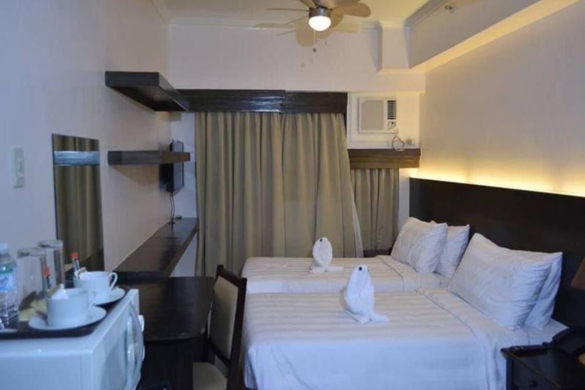 A hotel room with two beds, a desk with a microwave, a ceiling fan, and a window with curtains.