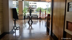 Een hotel lobby met een gepolijste marmeren vloer, een bloemstuk in het midden en uitzicht op de straat.