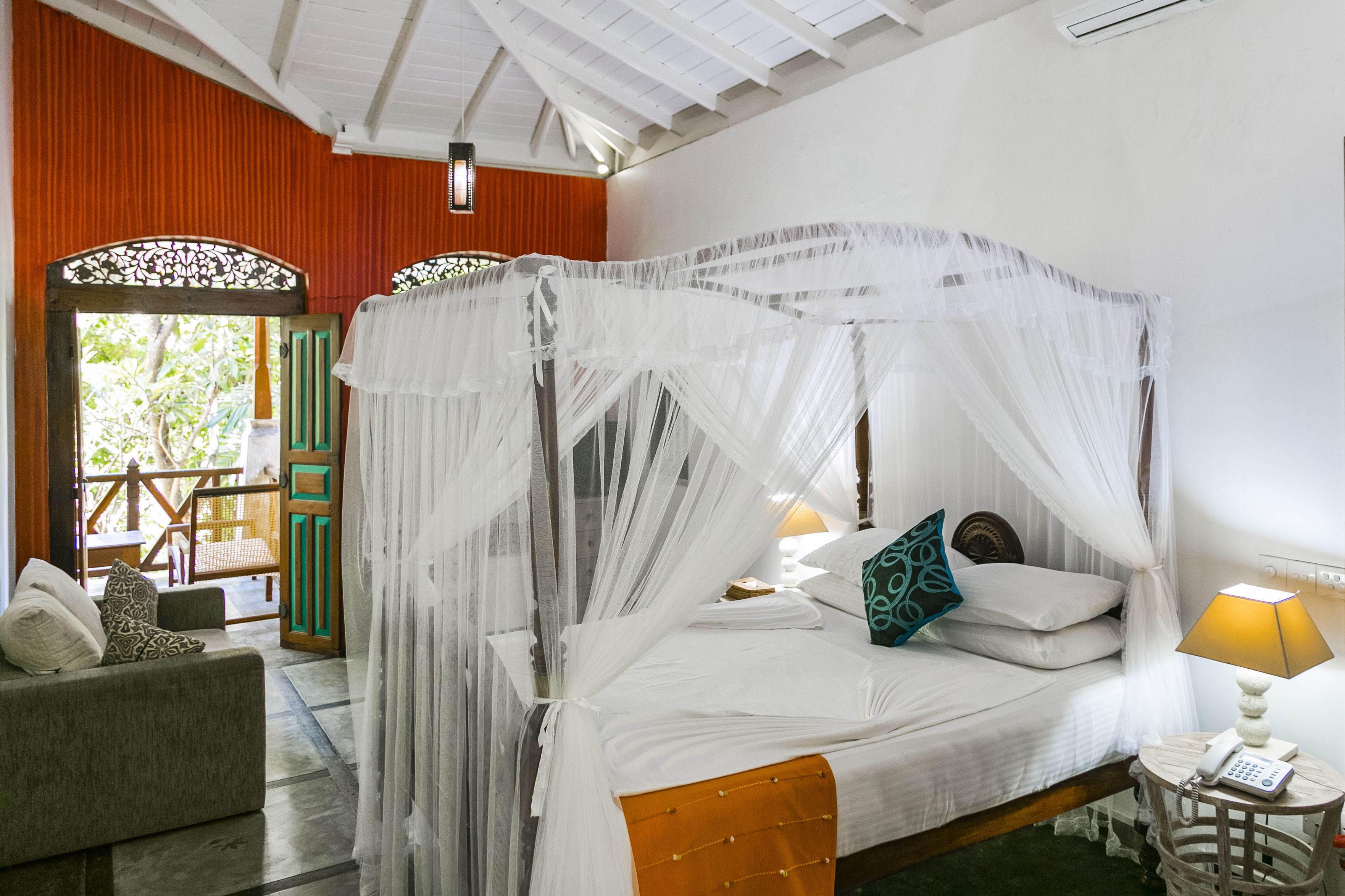 A four-poster bed with a canopy, a small bedside table with a lamp, and a sofa with cushions.