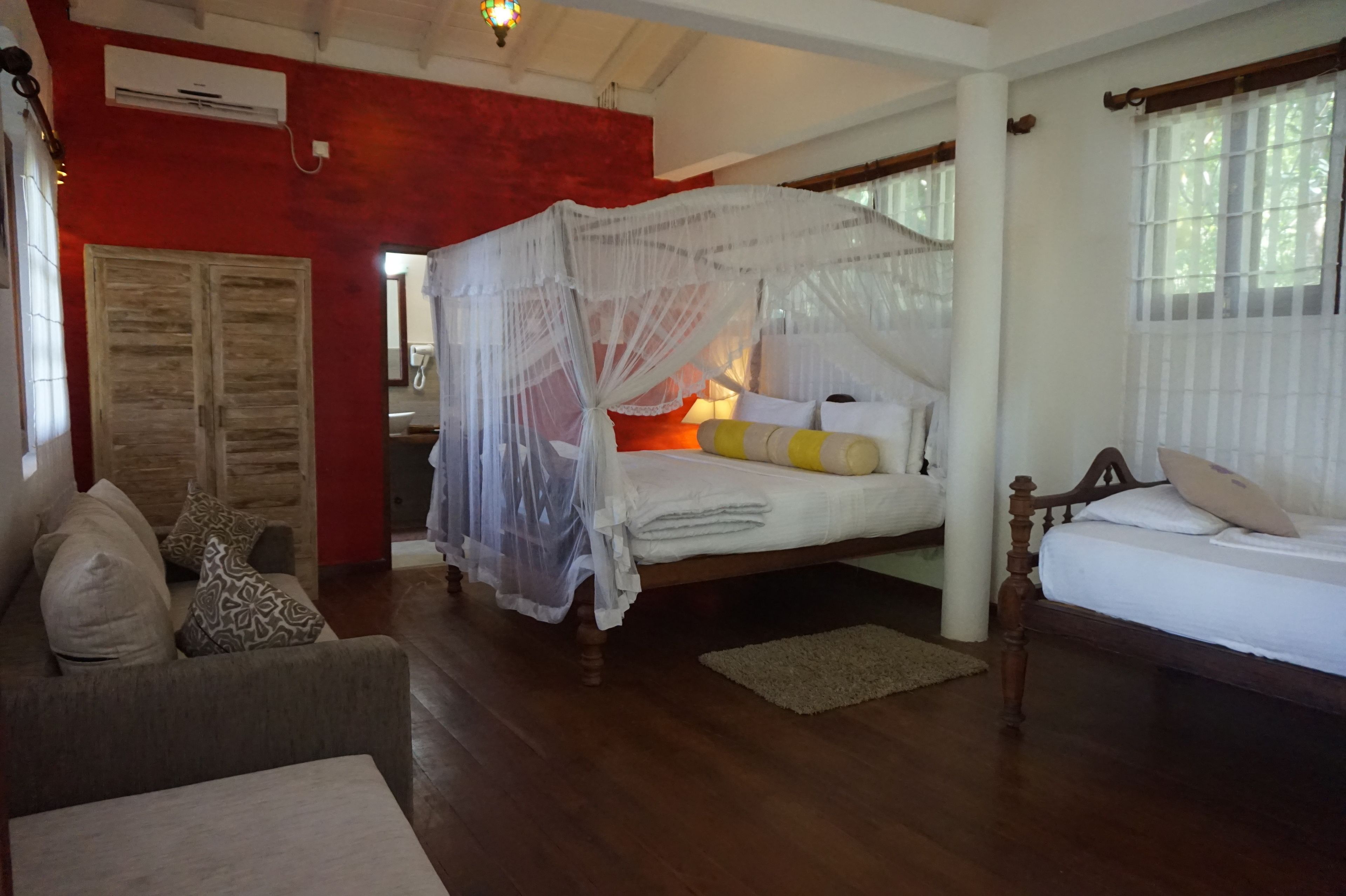 A bedroom with a bed, a nightstand, a wooden wardrobe, and a sitting area with a sofa and cushions.