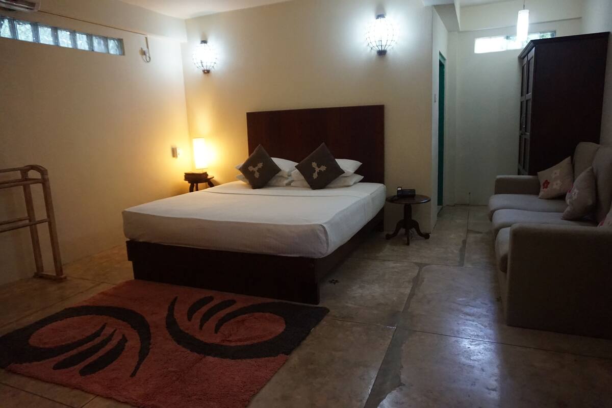 A hotel room with a bed, bedside table, lamp, and a sofa.