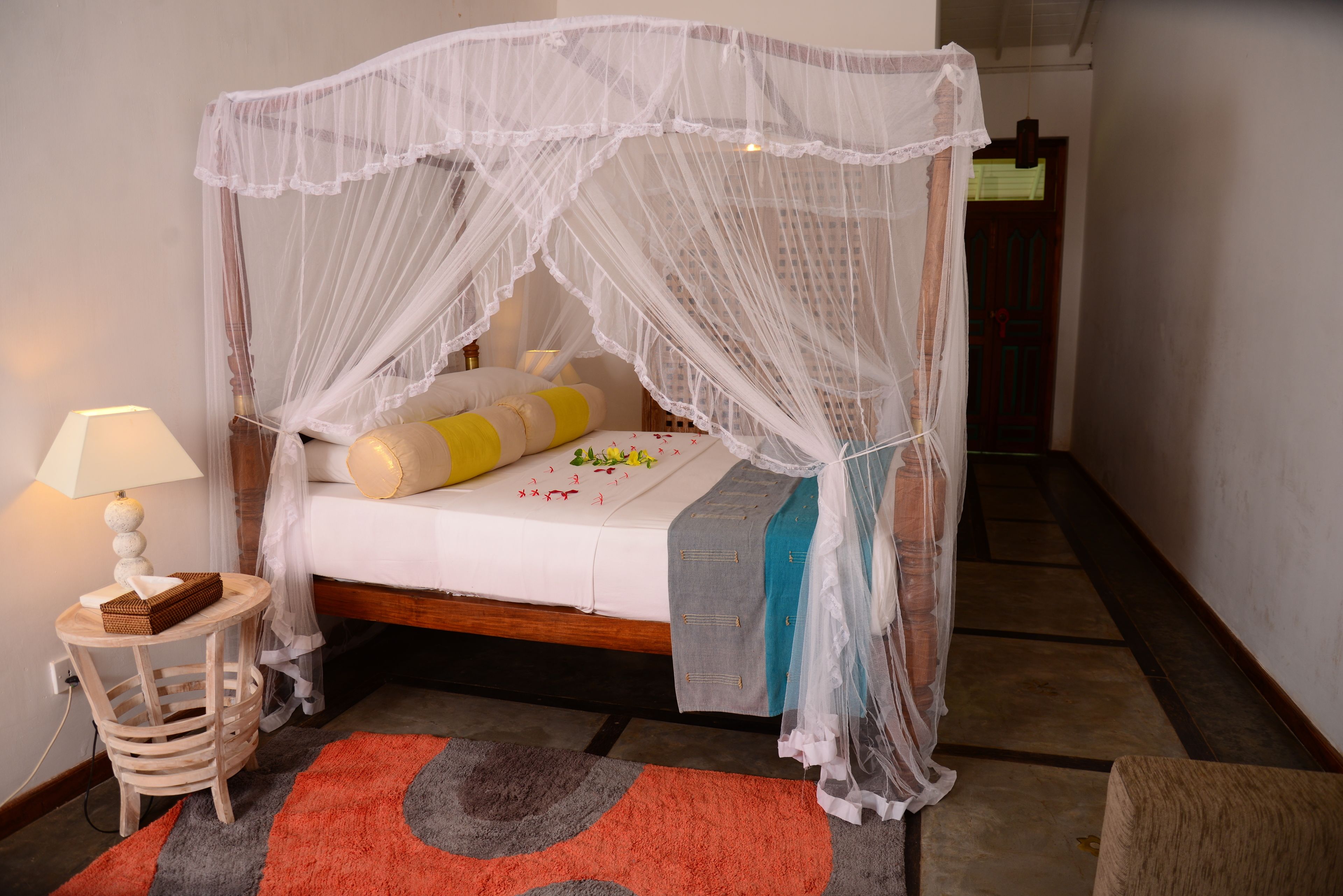 A bedroom with a canopy bed, a bedside table with a lamp, and a rug.
