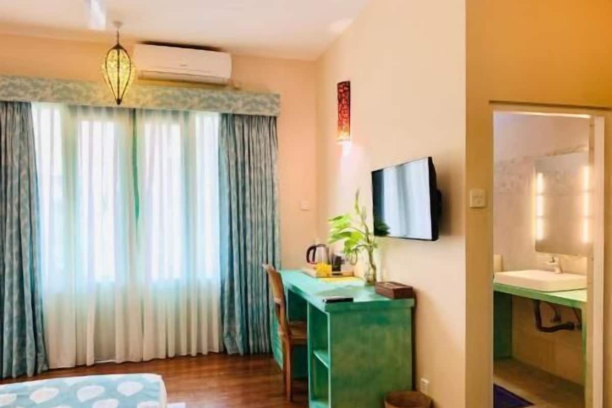 Quarto de hotel com cama, escrivaninha, cadeira, televisão e banheiro.