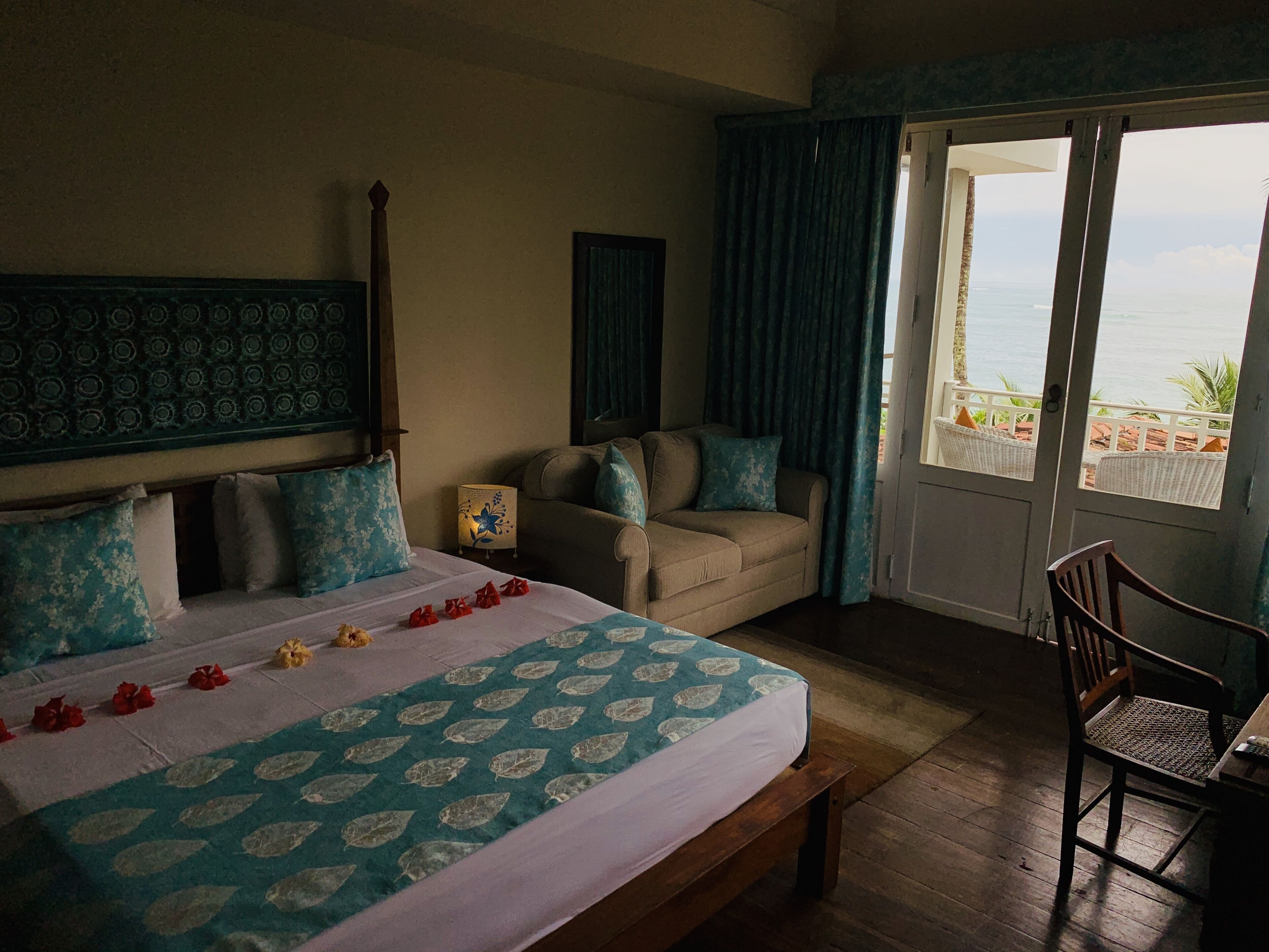 Een hotelkamer met een bed, een bank, een stoel en uitzicht op de oceaan door een groot raam.
