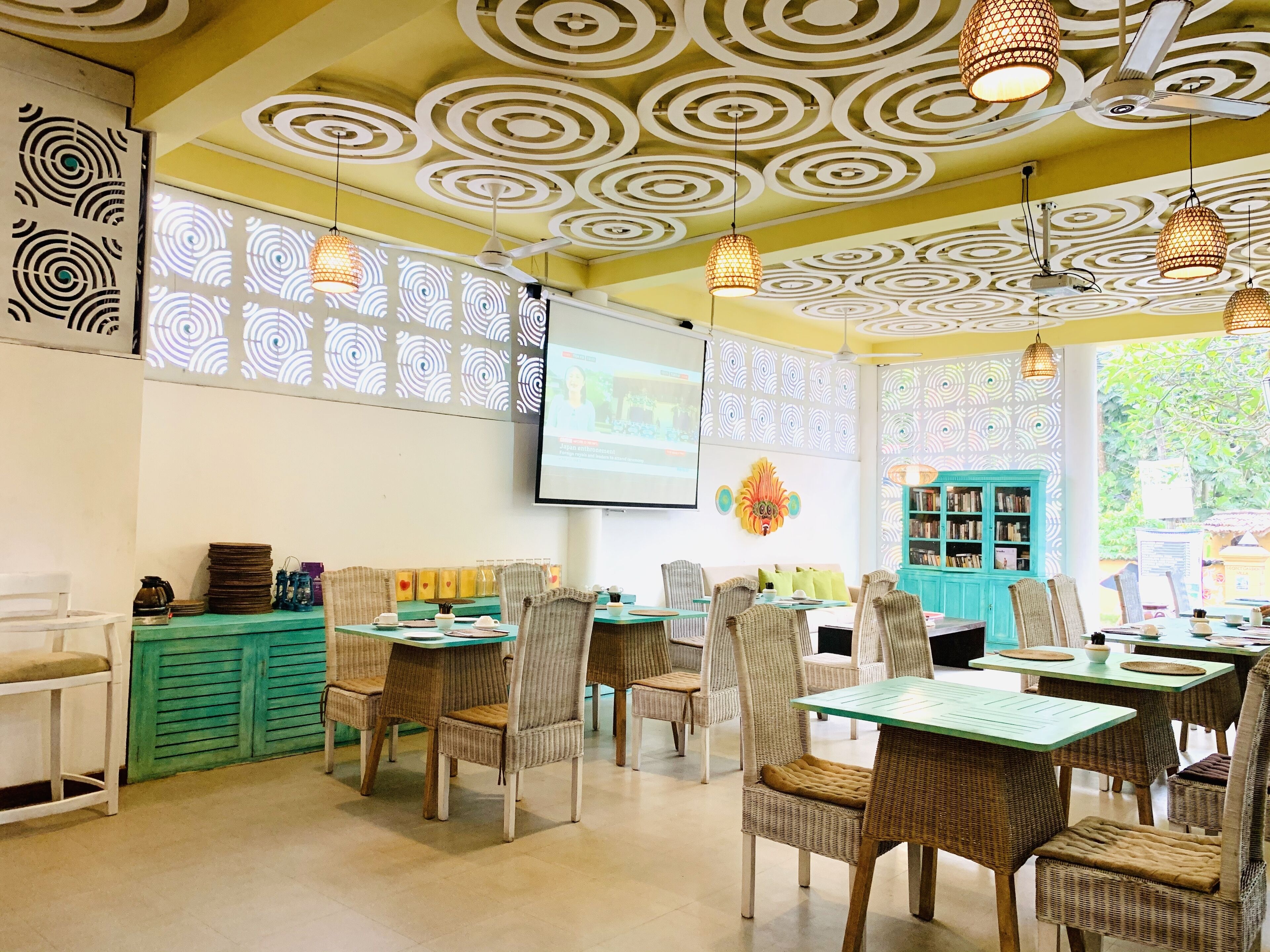 A cozy cafe with wicker furniture, a projector screen, and a patterned ceiling.