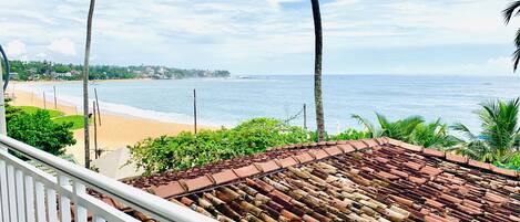 Vista de la playa desde un balcón con techo de tejas y barandilla blanca.
